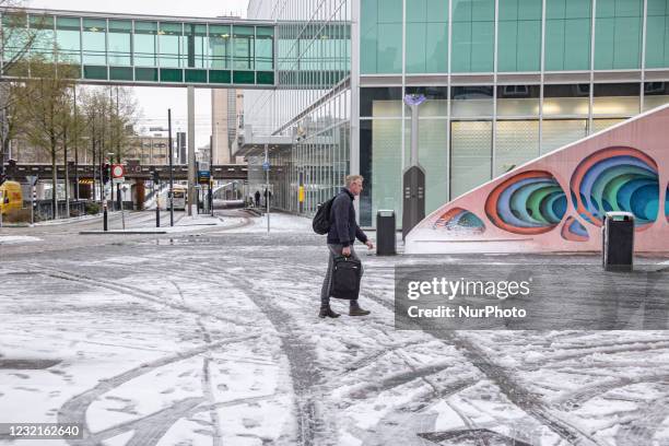 Man holding baggage as seen walking on the melting snow in Einhdoven city center square. The third day of the unusual April snowfall in The...