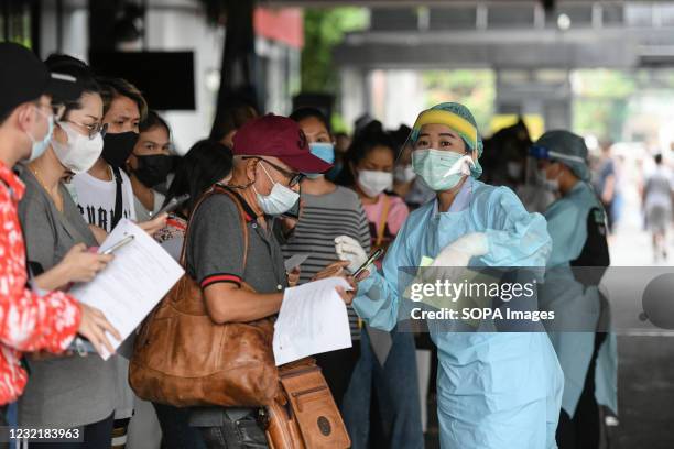 Health worker wearing a personal protective equipment suite assisting a woman in a queue for verification of his documents during a swab test drive...