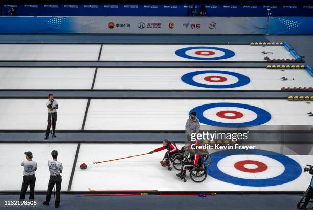 Chinese curler Shao Sheng Ping, center, throws a rock as teammate Yan Zhou assists and Chen Jian Xin, right, looks on during the wheelchair curling...