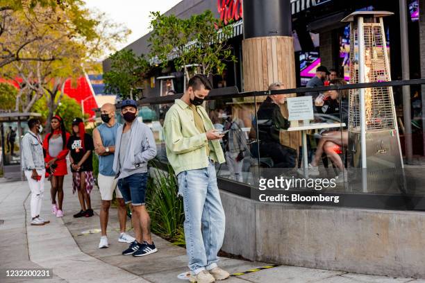 People wearing protective masks wait in line to eat at a restaurant in West Hollywood in Los Angeles, California, U.S. On Thursday, April 8, 2021....