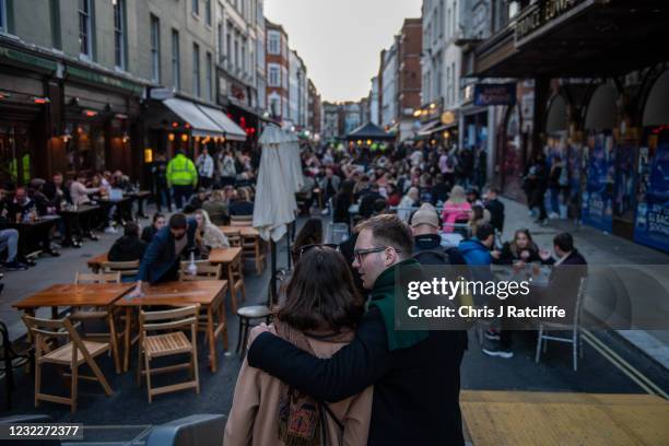 Couple embrace in front of a street of people eating and drinking in Soho as non essential retail reopens on April 12, 2021 in London, United...