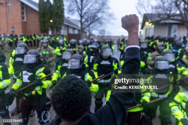 Man raises his fist as he faces the Minnesota State Troopers standing guard outside the Brooklyn Center Police Station after a police officer shot...