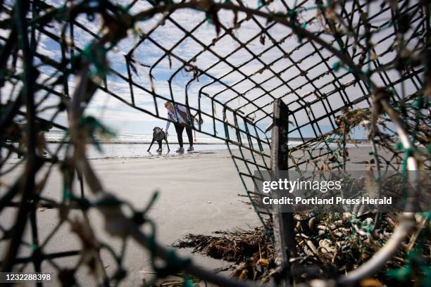 Seen through a lobster trap that washed ashore, a woman and a dog walk on Long Sands Beach in York on Thursday, April 8, 2021.