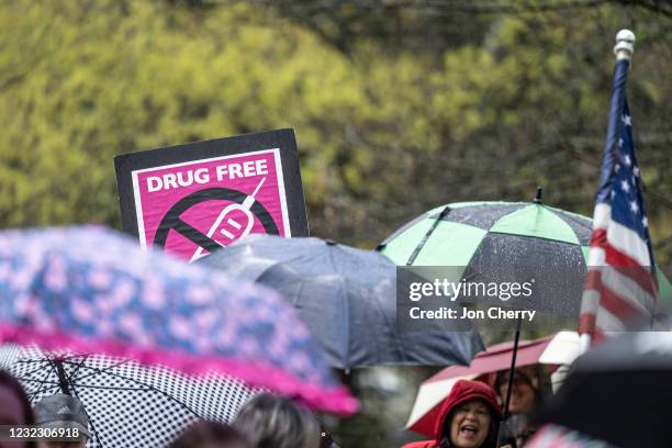 An anti-vaccination sign is seen above a row of umbrellas while demonstrators chant with speakers during a protest on state capitol grounds on April...