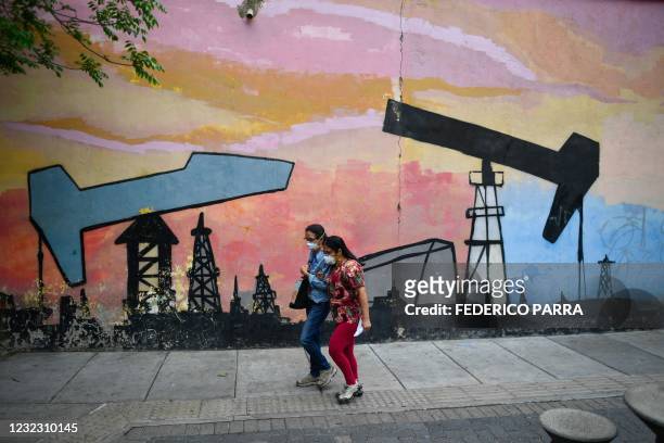 Women wearing a face masks walk past a mural depicting an oil pump in a street of Caracas, on April 14, 2021. - Amid crisis, hiperinflation, fall of...