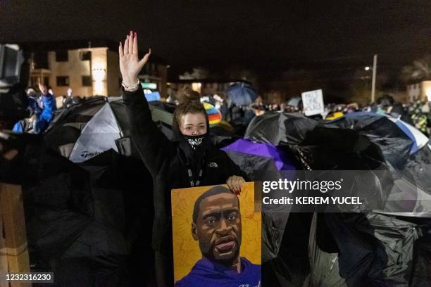 Demonstrator holding a poster of George Floyd, raises her hand towards a line of police officers outside the Brooklyn Center police station while...