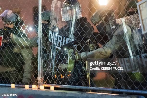 Hennepin County Sheriff Officer aims a riot weapon through a chain link fence as protesters rally outside the Brooklyn Center police station to...