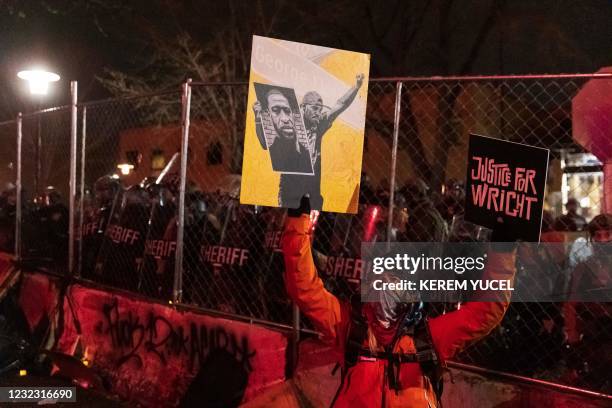 Demonstrator holding a poster of George Floyd and sign reading "Justice for Wright" in front of a line of police officers outside the Brooklyn Center...