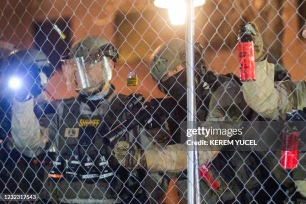 Hennepin County Sheriff Officer aims a riot weapon through a chain-link fence as protesters rally outside the Brooklyn Center police station to...