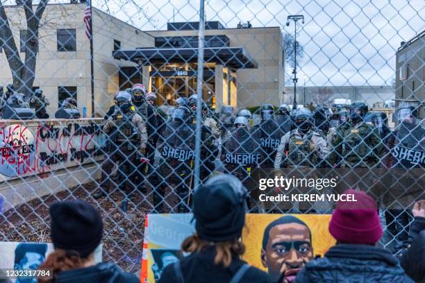 Sheriff officers stand guard outside the Brooklyn Center police station as demonstrators stand on the other side of the chaink-link fence protesting...
