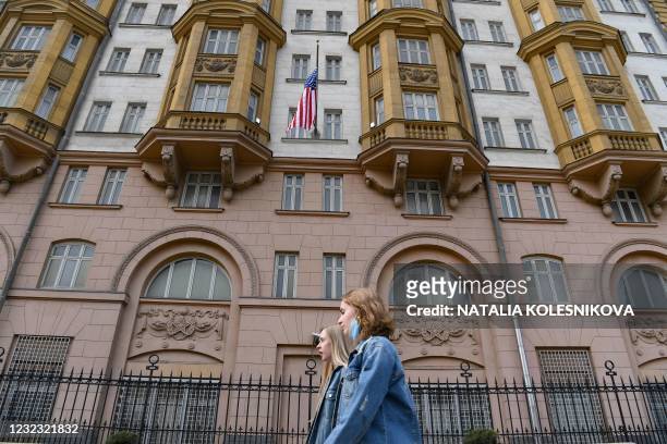 Two young women walk past the US embassy building in Moscow on April 15, 2021. - The United States announced economic sanctions against Russia on...