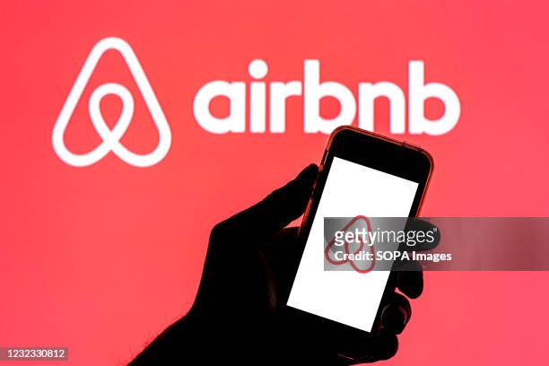 In this photo illustration, the Airbnb app seen displayed on a smartphone screen with the Airbnb logo in the background.