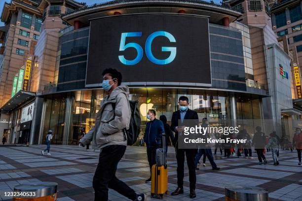 People stand in front of an Apple store advertising 5G capable phones on April 16, 2021 at a shopping district in Beijing, China. China announced...
