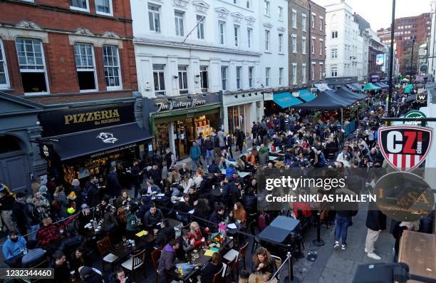 People sit at outside tables to eat and drink at re-opened bars and restaurants, in the street in the Soho area of London, on April 16, 2021...