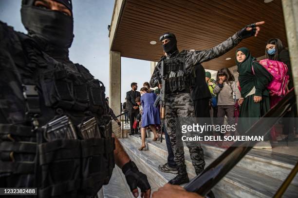 Members of Syrian Kurdish security forces motion to each other while children walk out of a building, during the handover of orphaned children, whose...