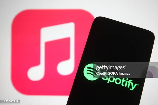 In this photo illustration, the Spotify logo seen displayed on a smartphone screen in front of Apple Music logo in the background.