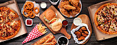 Table scene of assorted take out or delivery foods, top down view on a dark wood banner
