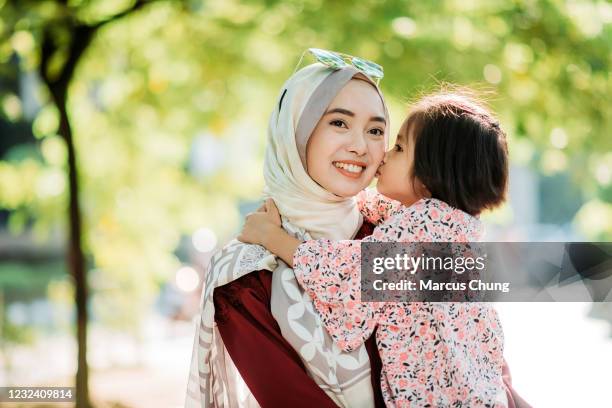 asiatische junge malay tochter küsst ihre mutter wange, während lächelnde mutter hält sie auf der stadt straße - malaysian culture stock-fotos und bilder