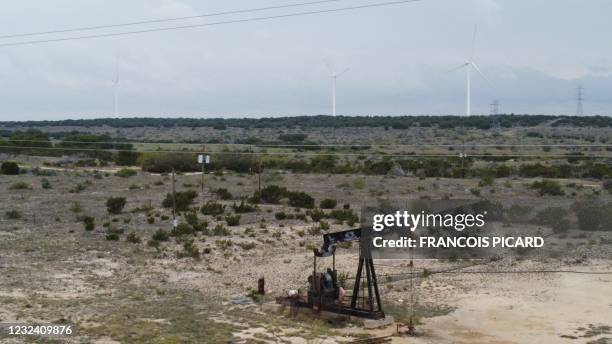 Blades from wind turbines rotate in a field behind an out of use oil pumpjack, April 16, 2021 near Eldorado, Texas. - Cattle rancher Bobby Helmers...