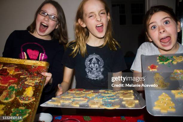 three pre teen girls holding baking sheets filled with christmas cookies and making goofy faces at the camera. - looking back stock-fotos und bilder