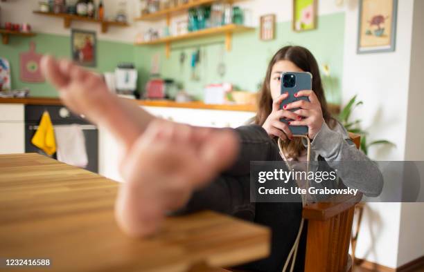 Bonn, Germany In this photo illustration a girl with her smartphone sits in a kitchen with feet on a table on April 16, 2021 in Bonn, Germany.