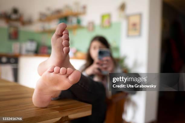 Bonn, Germany In this photo illustration a girl with her smartphone sits in a kitchen with feet on a table on April 16, 2021 in Bonn, Germany.