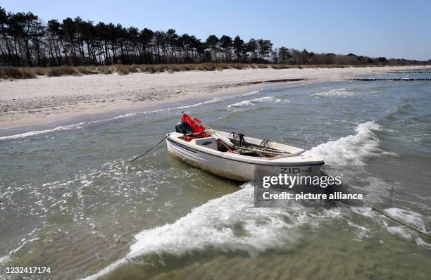 April 2021, Mecklenburg-Western Pomerania, Zingst: The beach of the Baltic resort is almost deserted, while an angler's boat is anchored on the...