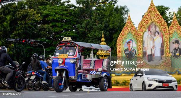 Tuk tuk drives past portraits of the Thai royal family in Dusit district. Thailand's internationally famous classic Tuk Tuk taxi. The three-wheeled...