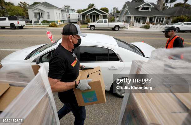 Volunteer carries a box of food to a car at a Food Bank of Santa Barbara County distribution site in Carpinteria, California, U.S., on Wednesday,...