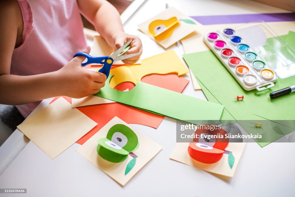 Little girl cutting colorful paper at the table.