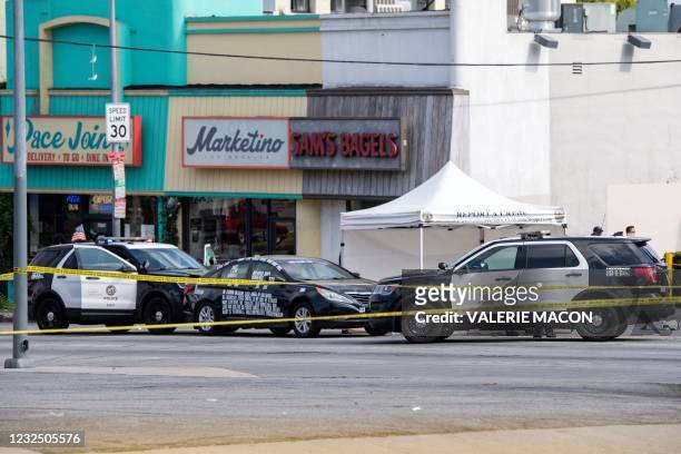Black vehicle covered with stickers is cornered by police cars at the corner of Fairfax Avenue and Sunset Boulevard where a body covered in a white...