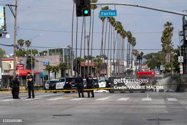 Police officers stand at the corner of Fairfax Avenue and Sunset Boulevard where a body covered in a white sheet lies on the pavement in Los Angeles...