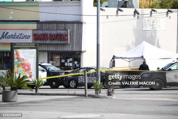 Black vehicle covered with stickers is trapped by police cars at the corner of Fairfax Avenue and Sunset Boulevard where a body covered in a white...