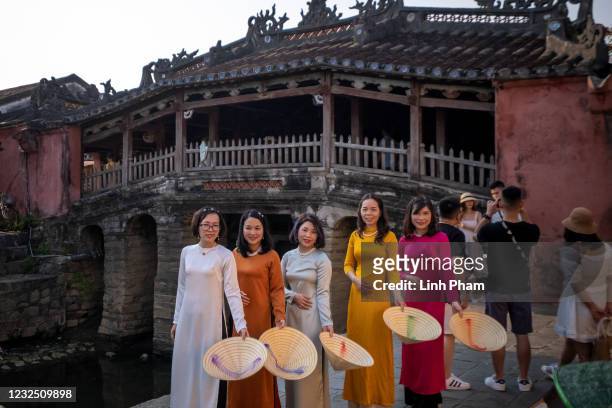 Women in traditional 'áo dài' and conical hats, pose for photos in front of the famous Japanese Covered Bridge in Hoi An ancient town on April 24,...