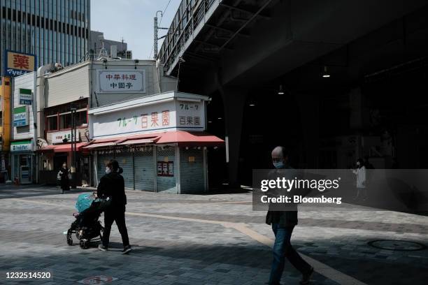 Pedestrians wearing protective masks walk past a shuttered fruit stand in the Yurakucho District of Tokyo, Japan, Sunday, April 25, 2021. Japanese...