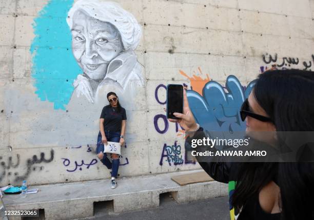 Young Lebanese woman takes a photograph of another in front of a newly painted portrait of the late Egyptian writer and feminist Nawal el-Saadawi on...