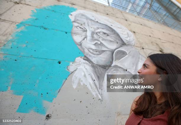 Young Lebanese woman gases at a newly painted portrait of the late Egyptian writer and feminist Nawal el-Saadawi on a wall in the capital Beirut's...