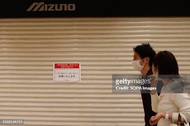 Couple walk in front of a large shopping center with shutters closed during a temporary holiday in Ginza. On the 25th of the first day when the third...