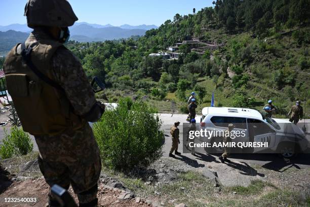 Pakistani soldier stands guard on a post as a vehicle carrying UN military observers arrives to visit near the Line of Control, de facto border...