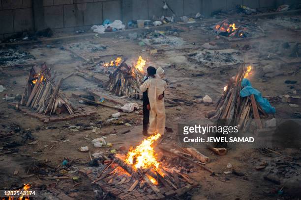 Family members embrace each other amid burning pyres of victims who lost their lives due to the Covid-19 coronavirus at a cremation ground in New...