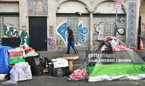 Man walks past tents housing the homeless on the streets in the Skid Row community of Los Angeles, California on April 26, 2021. - A federal judge...