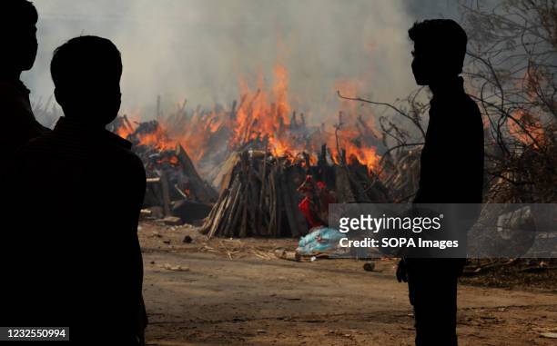 Family members look on as several funeral pyres of those patients who died of COVID-19 disease burn up during the mass cremation at Ghazipur...