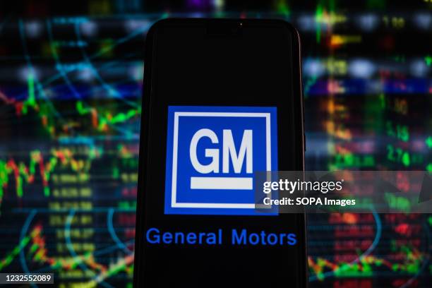 In this photo illustration a General Motors logo seen displayed on a smartphone with stock market percentages in the background.