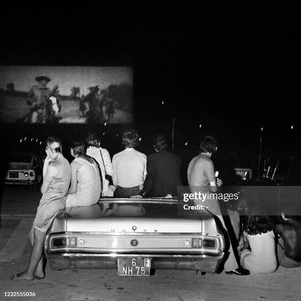 Group of people sit in and lean on a Buick convertible car as they watch an unidentified cowboy movie at the Rungis drive in, in Paris on August 6,...