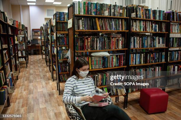 Girl wearing a facemask as a preventive measure against the spread of covid-19 reads a book in the subscription hall in the Pushkin Library in...