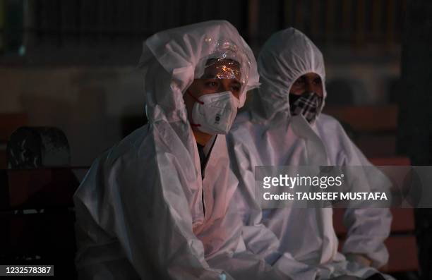Relatives in personal protective equipment suits watch the cremation of their loved one who died of the Covid-19 coronavirus at Nigambodh Ghat...