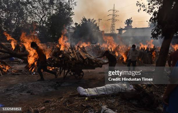 Workers carry wood amid burning funeral pyres of Covid-19 victims during a mass cremation, at Gazipur crematorium on April 28, 2021 in New Delhi,...