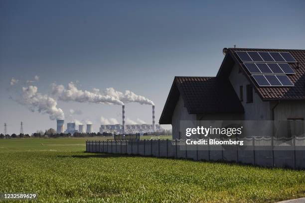 Solar panels on residential property rooftop near vapor rising from chimneys at the Belchatow coal powered power plant, operated by PGE SA, in...