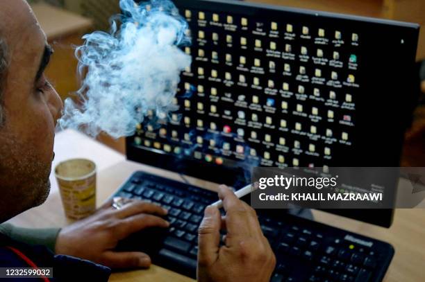 Jordanian man smokes a cigarette as he checks his computer in the Jordanian capital Amman, on March 26, 2021. - With already one of the world's...