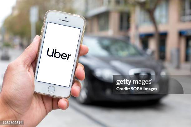 In this photo illustration a Uber logo seen displayed on a smartphone screen with a car in the background.